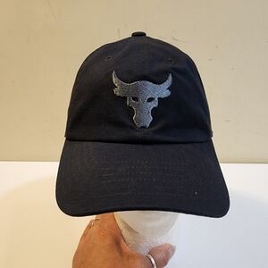 Under Armour Project Rock Trucker Hat in black with the  Gray Bull Logo